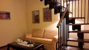 A living room with a sofa, a coffee table, and a staircase with a railing. - Castello Izzalini Todi Resort "Apt 4" (Izzalini)