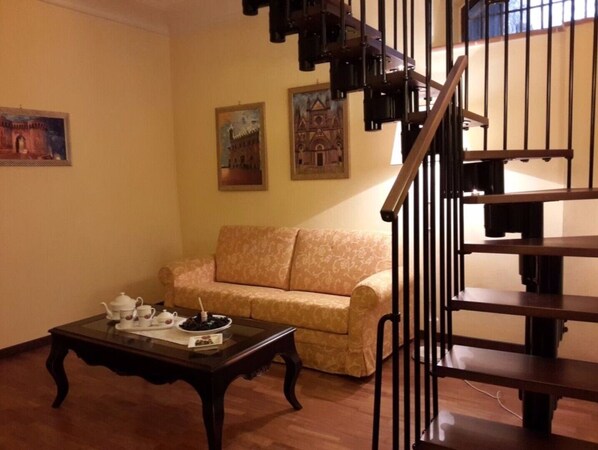 A living room with a sofa, a coffee table, and a staircase with a railing. - Castello Izzalini Todi Resort "Apt 4" (Izzalini)