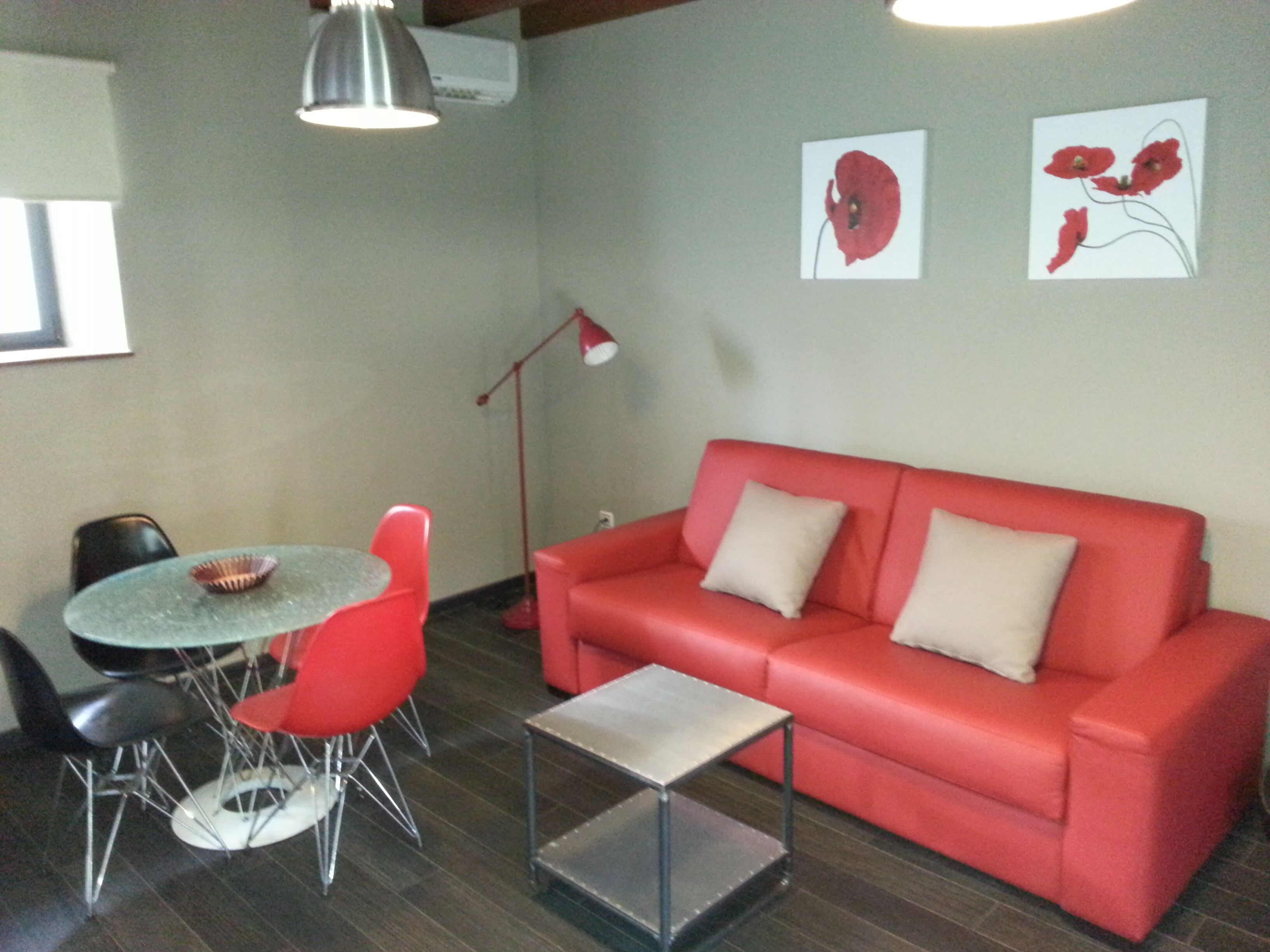 A room with a red sofa, a round table with two chairs, a small square table, and two wall-mounted artworks.