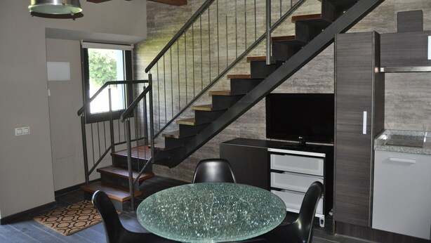 A modern kitchen with a built-in stove, a dining area with a glass table, and a staircase leading to another level. - Rural apartment Casona la Sierra for 4 people (Cudillero)
