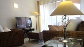 A living room with wicker furniture, a glass coffee table, a flat-screen TV, and a lamp. - Luxury Aptmt, Seaview Sunset, Large Pool, free Wi-Fi, UK-TV (Peyia)