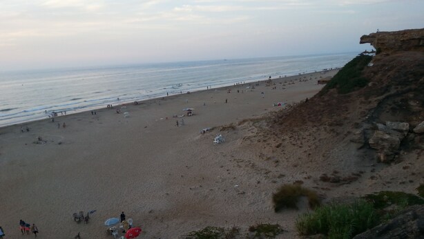 A beach with a rocky cliff on one side and a sandy shore with umbrellas and beach chairs. - Apartment in Tangier, by the sea with swimming pool and garage. (Tanger)
