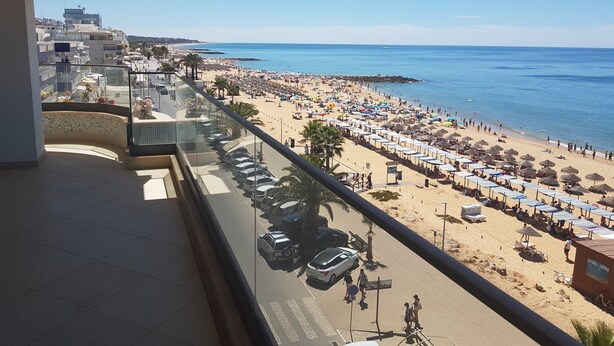 Een balkon met uitzicht op een strand, een parkeerplaats en een hotelschbord.