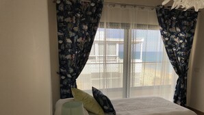 Een slaapkamer met twee bedden, een raam met dunne gordijnen en een lamp.