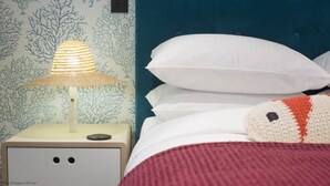 Un letto con cuscini bianchi e una coperta all'uncinetto, un comodino con una lampada e una parete con motivo corallo.