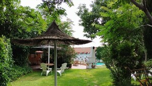 Un exuberante jardín con un pabellón de paja, mobiliario exterior y una zona de piscina.