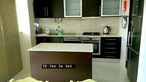 Una cucina compatta con mobili scuri, un'isola centrale, un lavello, fornello e frigorifero.