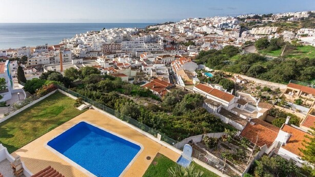 Vista aerea di una località costiera con una grande piscina circondata da vegetazione e edifici residenziali.