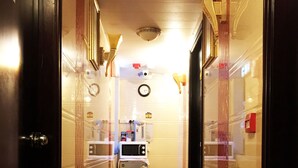 A hotel hallway with a marble floor, a clock on the wall, a refrigerator, and a trash bin. - Pacific Lodge (Kowloon)