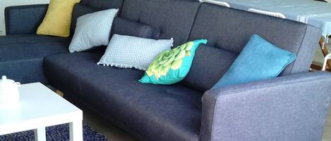 Un soggiorno moderno con un divano grigio, un piccolo tavolino bianco e un tappeto azzurro decorato.