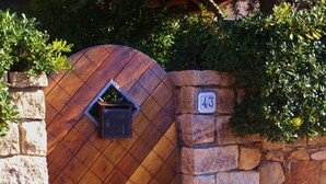 Een houten poort met een brievenbus, een stenen muur en een nummerbord.