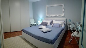 Een slaapkamer met een bed, kussens, een stoel, een nachtkastje en een garderobe.