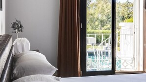 Et soveværelse med en stor seng, udsigt til det fri gennem en skydedør, og en lille balkon med gelænder i hvid.