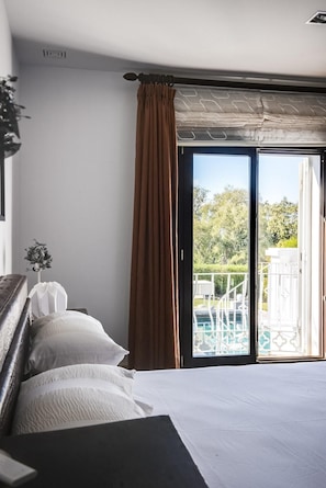 Een slaapkamer met een groot bed, uitzicht op het omliggende landschap door een schuifdeur, en een klein balkon met een witte reling.