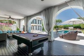 Een zwembadgedeelte met een pooltafel, buitenzitplaatsen en uitzicht op een huis.