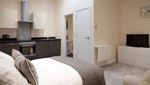 Une chambre avec un lit, une télévision, une armoire et un coin cuisine équipé de placards et d’une cuisinière.