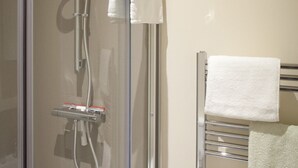 Une douche fermée par des parois en verre, dotée d’un pommeau de douche à main et d’un porte-serviettes avec deux serviettes.