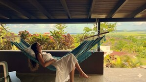 Una persona relajándose en una hamaca en un balcón con vistas a un paisaje exuberante.