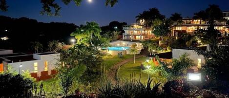 Et moderne resort med swimmingpool, frodig beplantning og flere bygninger.