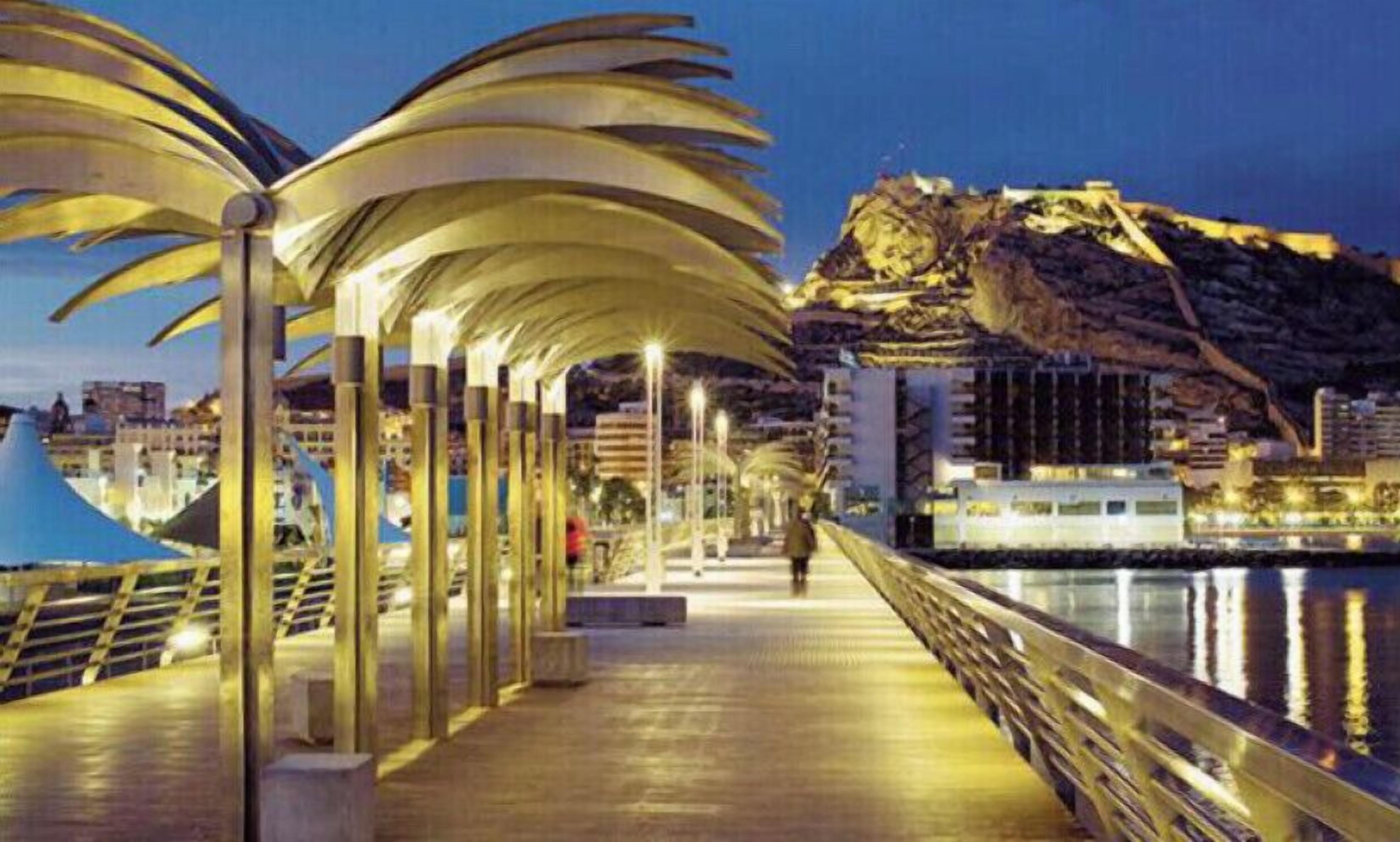 A waterfront promenade with a series of palm-like structures providing shade.
