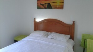 Una cama con cabecera de madera, ropa de cama blanca y un cuadro de un atardecer sobre un puente en la pared.