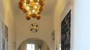 Un pasillo con suelo de baldosas, un aplique decorativo, un reloj y una puerta con reja de metal.