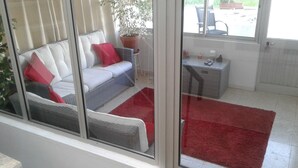 Una habitación con sofá, alfombra roja, una mesita y una planta en maceta.