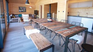 A spacious living area with a long wooden table, benches, and a sofa. There is a kitchen area with cabinets and a stove. - L' Edelweiss, luxury chalet with exceptional lake view, close to center/slopes (Gérardmer)