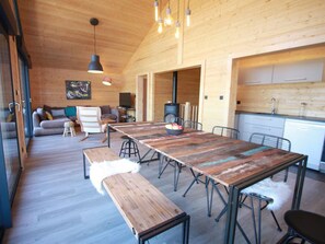 Un'ampia zona giorno con un lungo tavolo di legno, panche e un divano. È presente anche un angolo cottura con armadietti e fornelli.