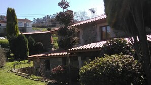 Une cour avec un bâtiment en pierre, une pelouse bien entretenue et une variété d’arbustes et d’arbres.