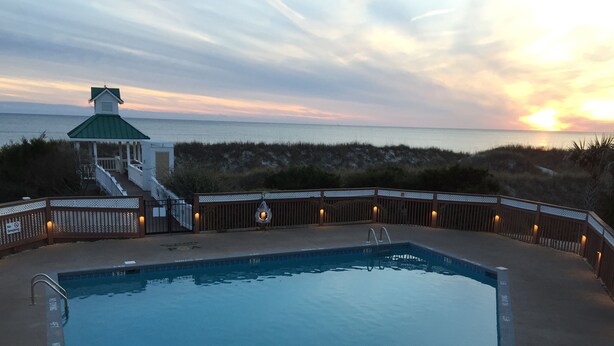 Una piscina con una torre de salvavidas y vistas a la playa al atardecer.
