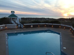 A swimming pool with a lifeguard tower and a beach view at sunset.