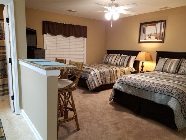 A bedroom with two beds, a dining table, and a ceiling fan.