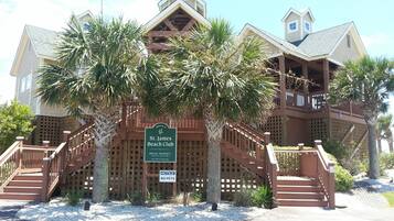 A two-story building with a wooden deck and stairs, surrounded by palm trees. A sign indicates it is the St. James Beach Club, private property, and no pets are allowed.
