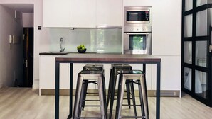 Een moderne keuken met een centraal eiland, roestvrijstalen apparatuur en een glazen deur naar een balkon.
