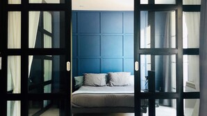 Een slaapkamer met een bed, een blauwe accentmuur en een groot raam.