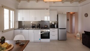 A modern kitchen with white cabinets, a built-in oven, a refrigerator, and a dining area with a wooden table and chairs. - Cycladic Breeze Villa Aura with swimming pool villa & great sea view  (Paros)