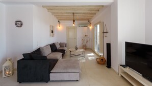 A modern living room with a sectional sofa, a flat-screen TV, and a wooden ceiling. - Cycladic Breeze Villa Aura with swimming pool villa & great sea view  (Paros)