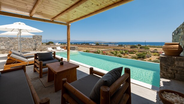 A wooden deck with a pool, lounge chairs, and a stone wall. - Cycladic Breeze Villa Aura with swimming pool villa & great sea view  (Paros)
