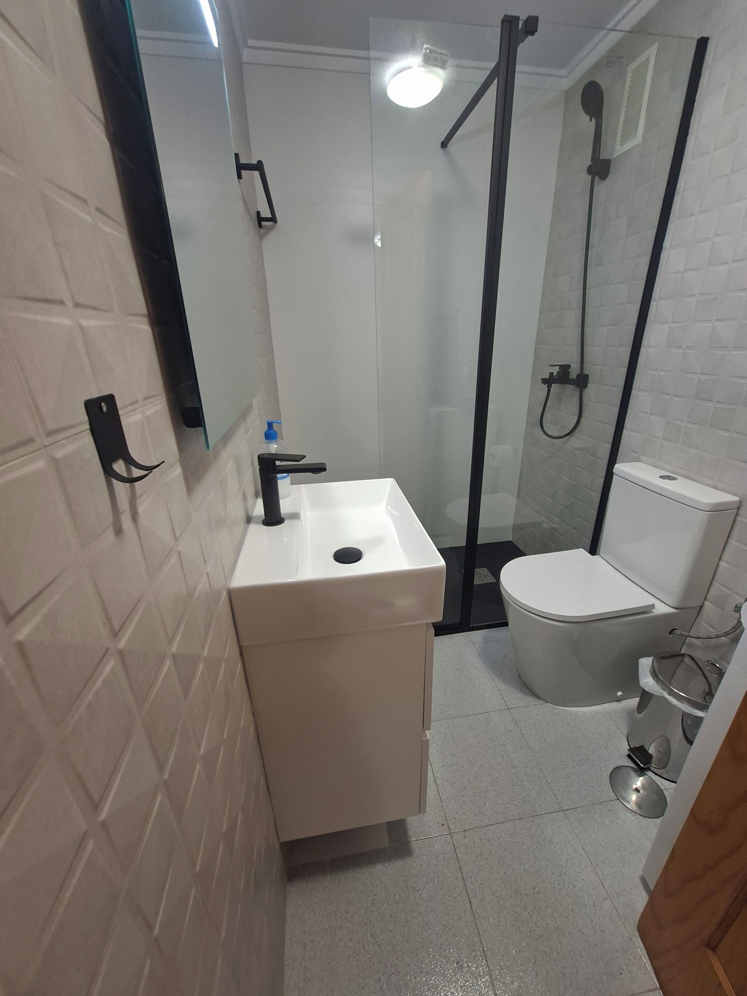 Casa de banho com lavatório branco, sanita e cabine de duche em vidro.