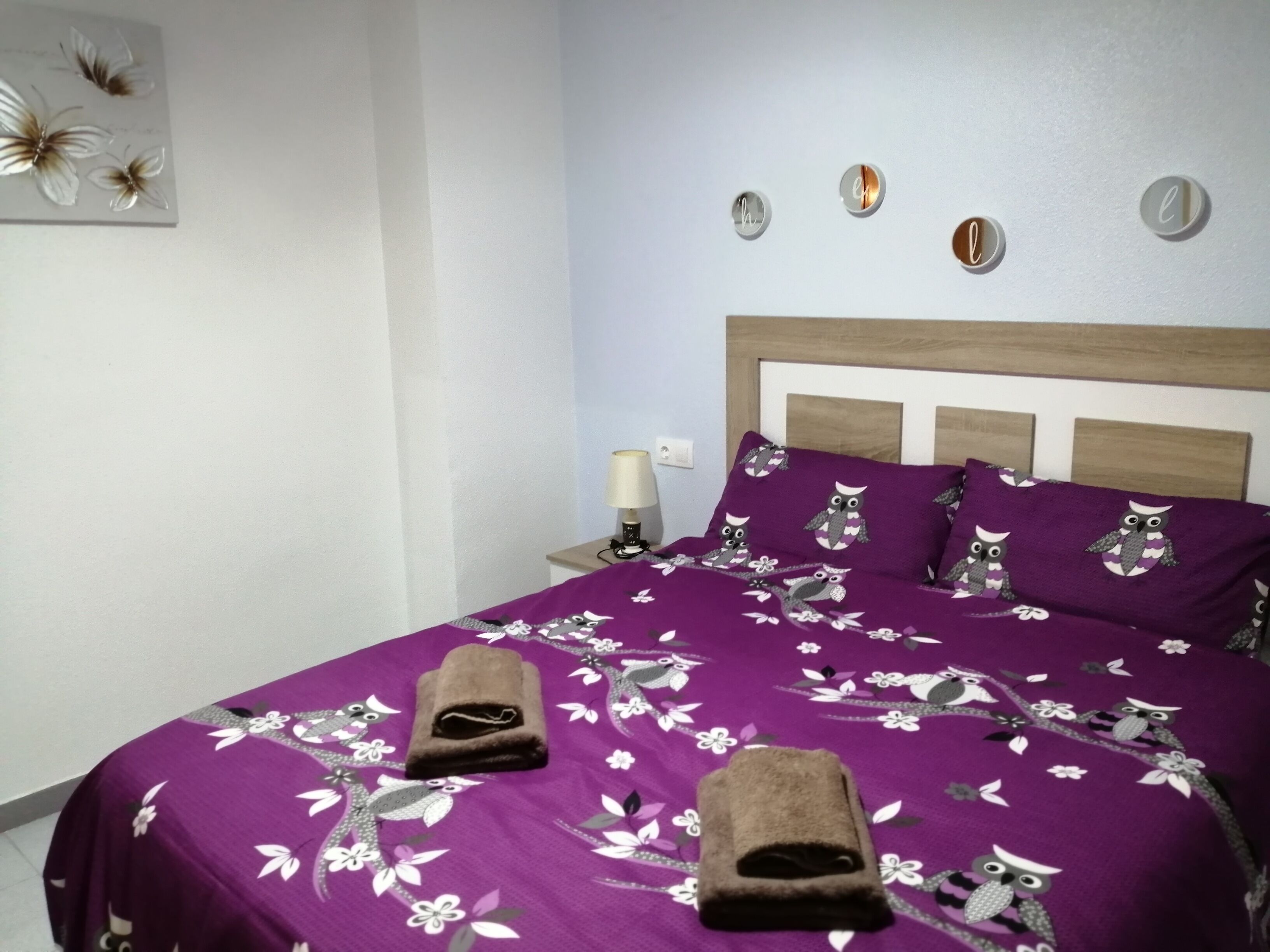 A hotel room with a bed, pillows, a nightstand, a lamp, and wall decorations.