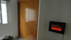 Ett rum med en garderob i trä, en platt-TV som visar en bild av en öppen spis och två handdukar på golvet.