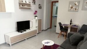 Ett modernt vardagsrum med en platt-TV, en soffa, en matplats med bord och stolar samt ett litet sidobord.