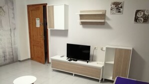 Ett modernt vardagsrum med en platt-TV placerad på ett TV-bord i trä, ett litet vitt bord, en grå soffa och ett träskåp.