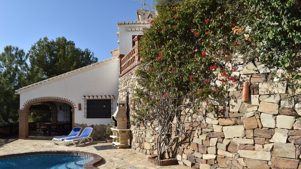 A pool area with a stone wall and a tree with red flowers. - Finca Almencino with private pool for 6 people, fantastic sea views (Cómpeta)