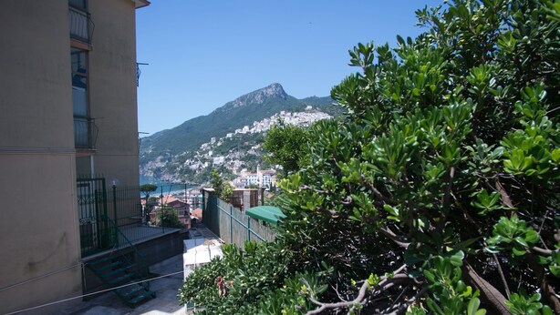 A building with a balcony, a staircase, and a view of a mountain and town in the background. - Vietri center "Villa Anna" (Vietri Sul Mare)