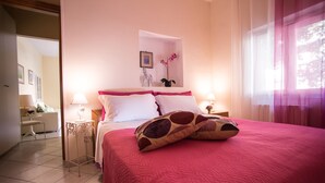 A bedroom with a large bed, two bedside tables with lamps, a small table with a lamp, a framed picture on the wall, and a window with curtains. - Vietri center "Villa Anna" (Vietri Sul Mare)