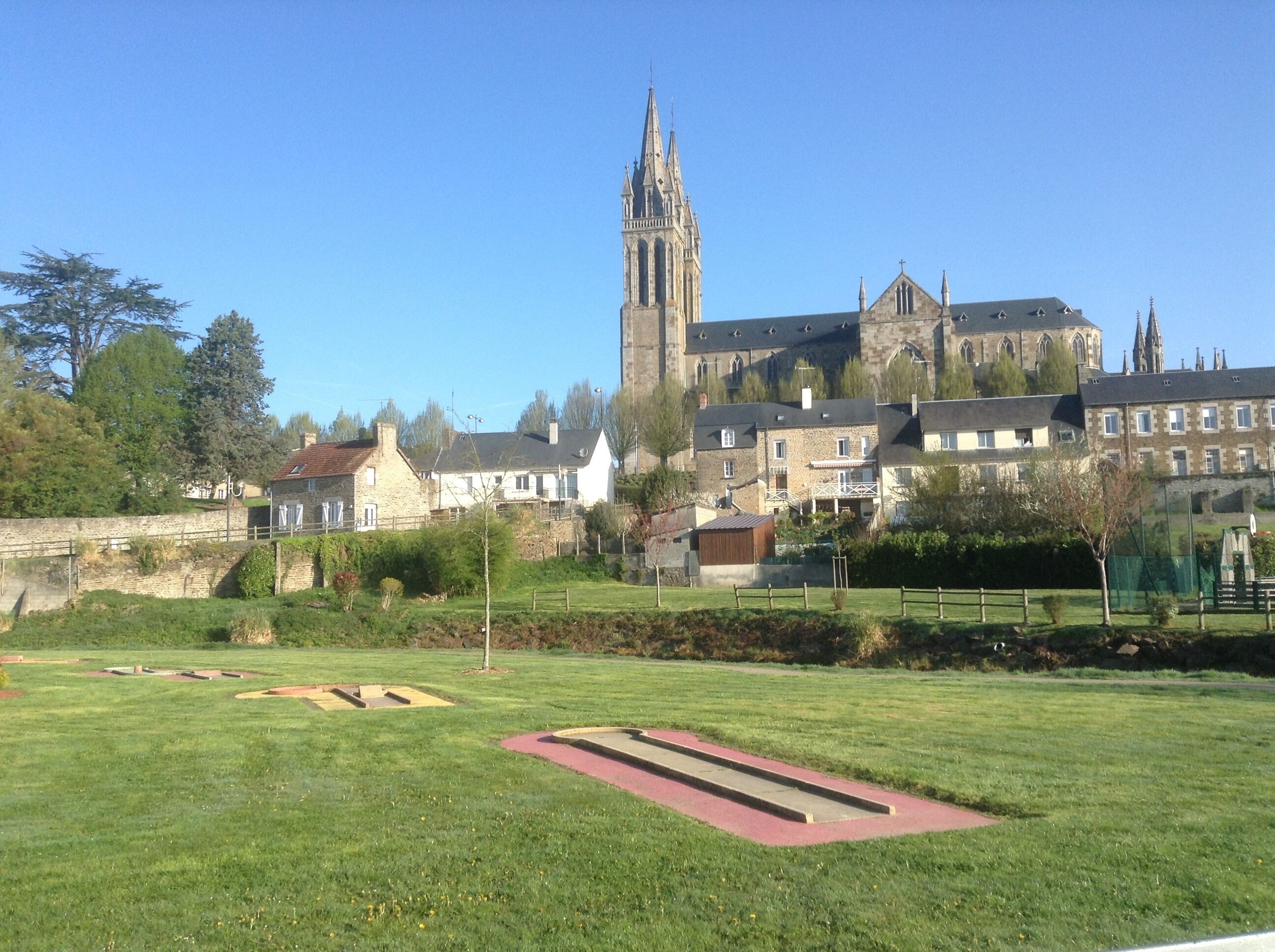 A grassy area with a red track, stone buildings, and a church with a tall spire in the background.