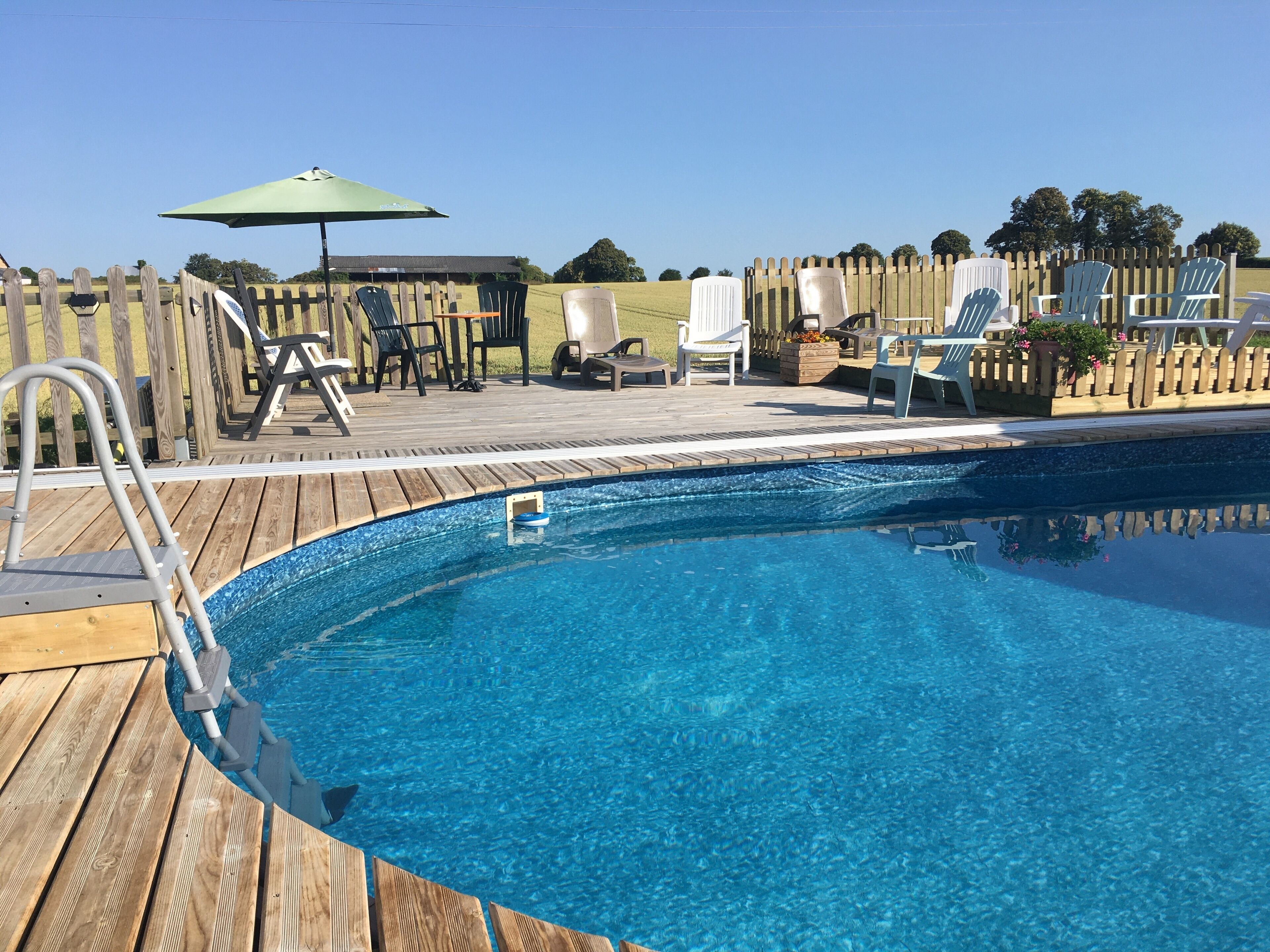 Una terraza de madera con piscina, sillas de descanso y un cerco de madera.