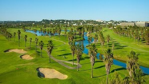 Ein Golfplatz mit Wasserhindernissen, Palmen und einem weit entfernten Gebäudekomplex.